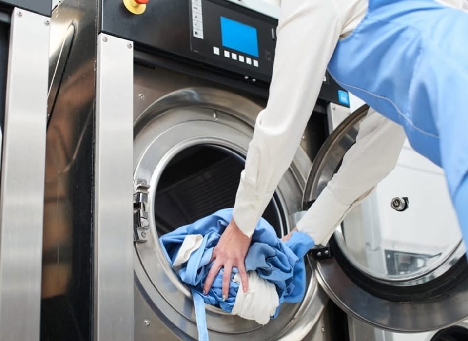 Laundry being loaded into a large commercial washing machine (illustrative photo)